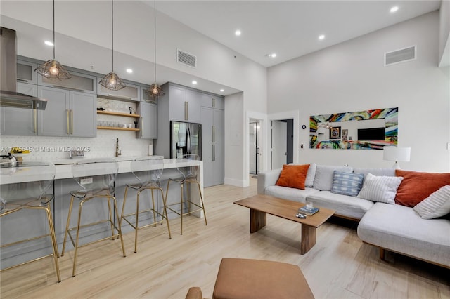 living room with indoor wet bar, light wood finished floors, a towering ceiling, and visible vents