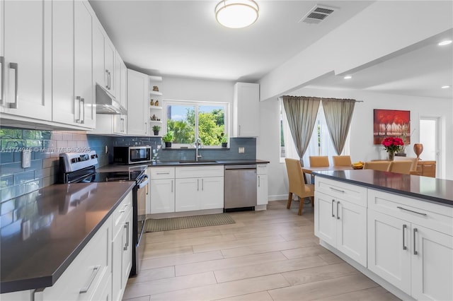 11215 NE 4th Ave, Miami, FL 33161 - kitchen with stainless steel appliances, under cabinet range hood, dark countertops, decorative backsplash, and white cabinets