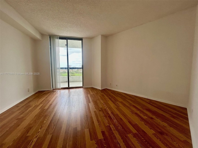unfurnished room featuring a textured ceiling, baseboards, expansive windows, and wood finished floors