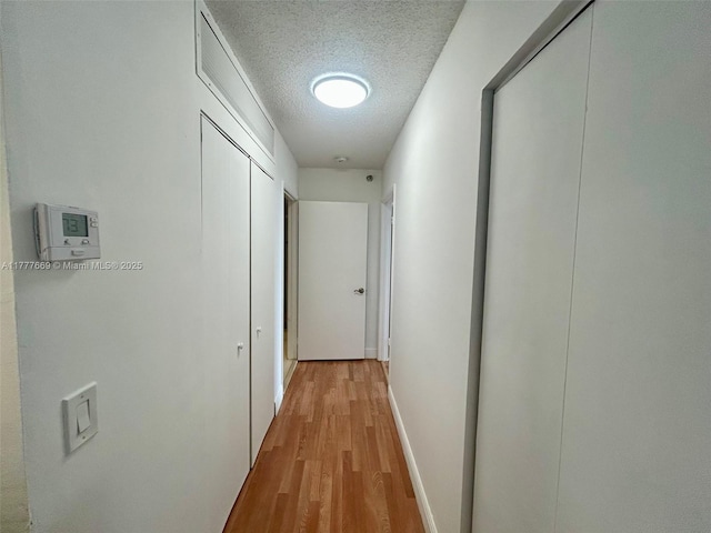 hall with baseboards, a textured ceiling, and light wood finished floors