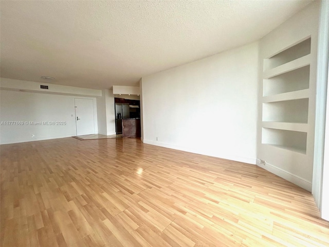 unfurnished living room with built in shelves, light wood finished floors, a textured ceiling, baseboards, and visible vents