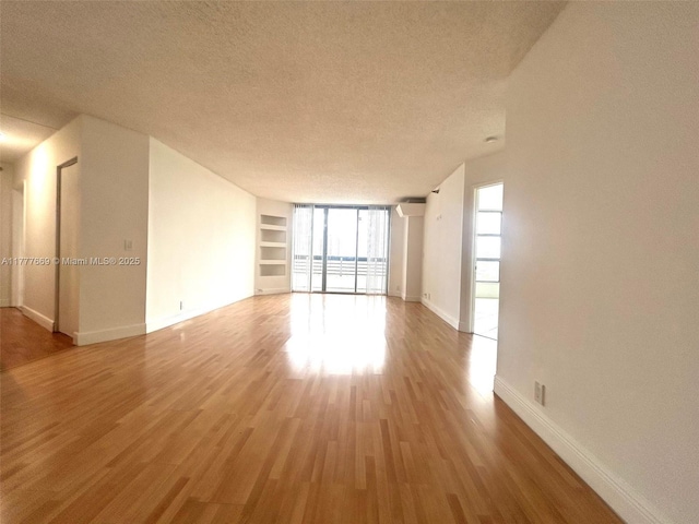 empty room with baseboards, wood finished floors, built in features, and a textured ceiling