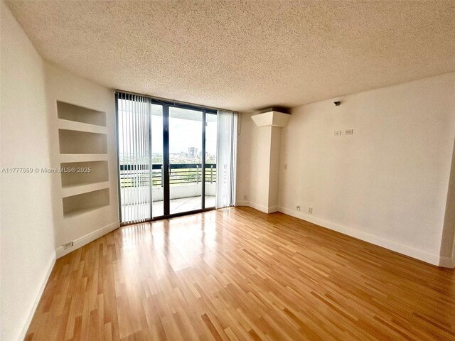 empty room featuring baseboards, expansive windows, a textured ceiling, and light wood finished floors