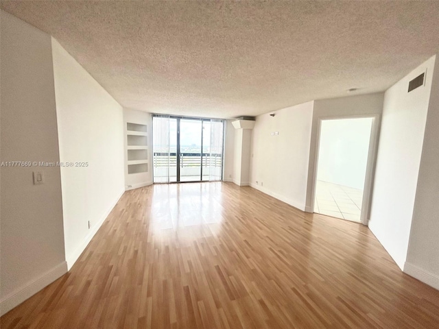 unfurnished room with built in shelves, wood finished floors, a textured ceiling, baseboards, and visible vents
