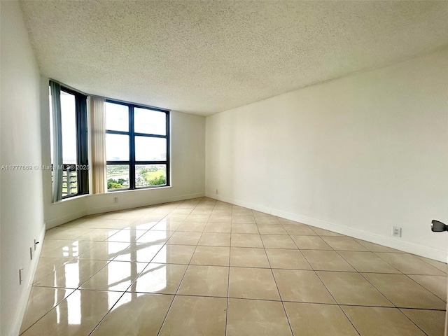 tiled empty room featuring baseboards and a textured ceiling