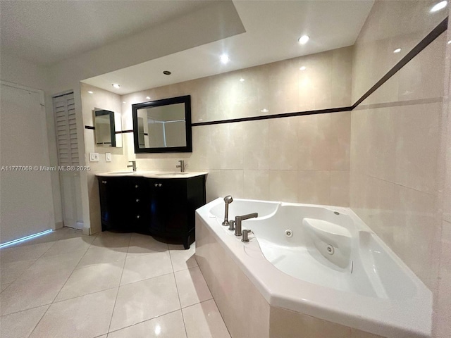 full bath featuring a sink, a tub with jets, double vanity, tile patterned flooring, and tile walls