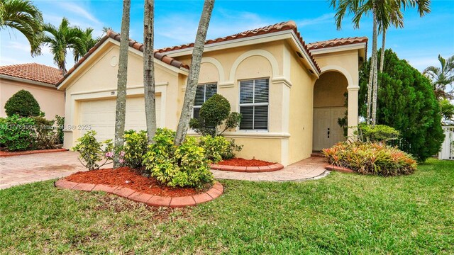 mediterranean / spanish house with a tile roof, driveway, an attached garage, a front yard, and stucco siding