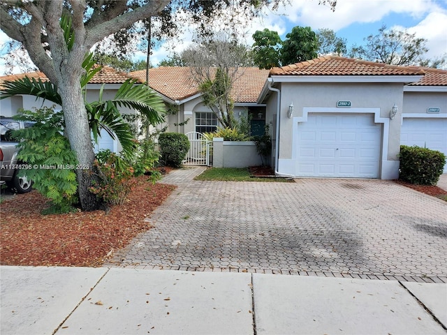 view of front of home featuring stucco siding, decorative driveway, a tile roof, a gate, and a garage