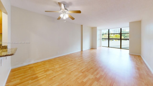 spare room featuring ceiling fan, baseboards, a wall of windows, and light wood-type flooring