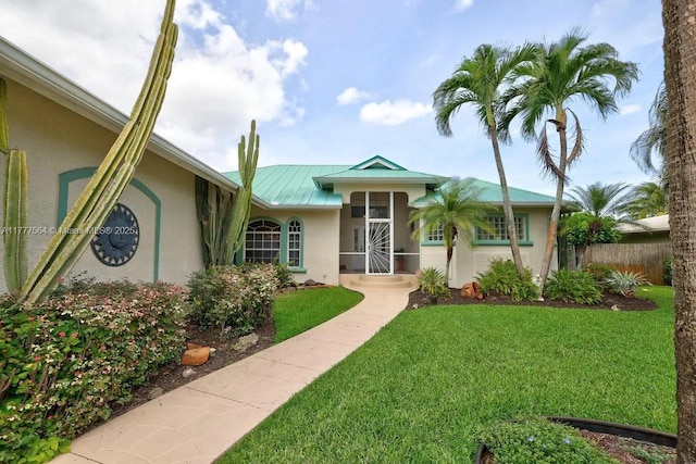 single story home with metal roof, stucco siding, fence, and a front yard