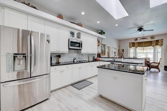 kitchen featuring tasteful backsplash, a peninsula, dark countertops, a skylight, and stainless steel appliances