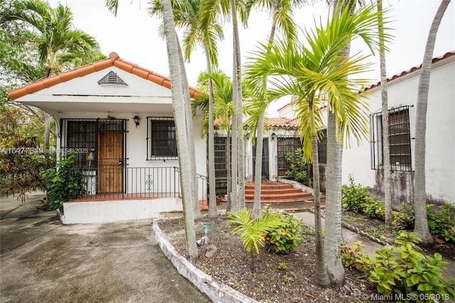 property entrance with stucco siding, covered porch, and a tiled roof