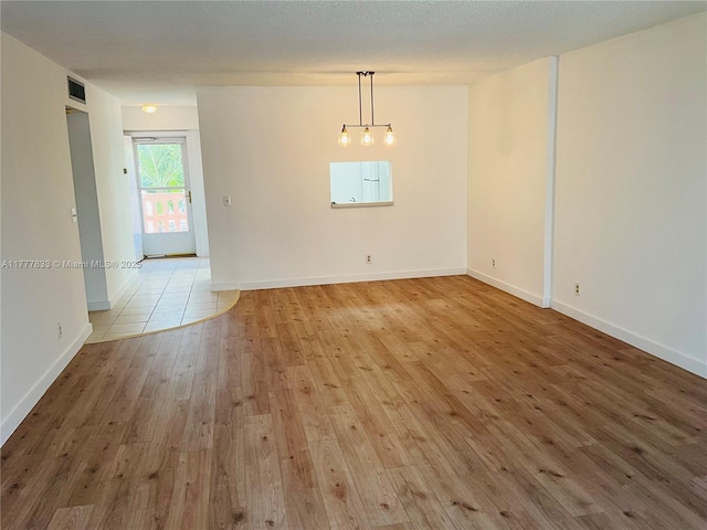 empty room with a chandelier, visible vents, baseboards, and hardwood / wood-style floors