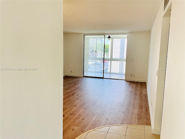 empty room with a wall of windows, wood finished floors, and baseboards