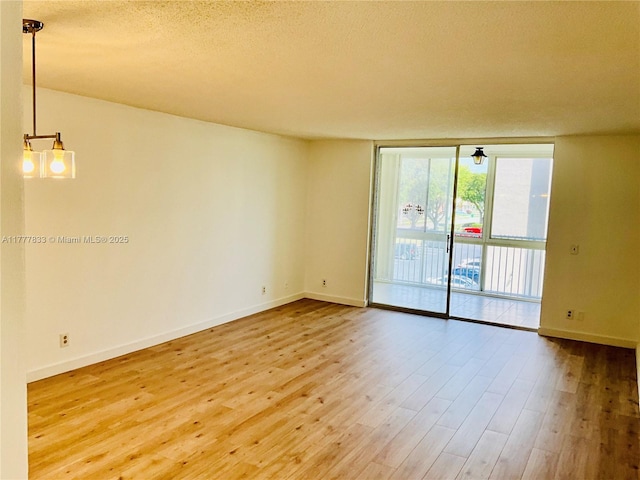 empty room featuring a textured ceiling, wood finished floors, floor to ceiling windows, and baseboards