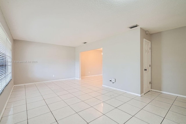 spare room with a textured ceiling, light tile patterned flooring, baseboards, and visible vents