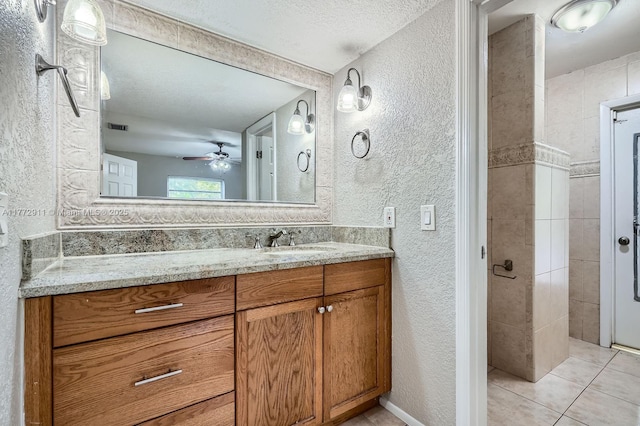 bathroom with a textured wall, tile patterned flooring, vanity, and ceiling fan
