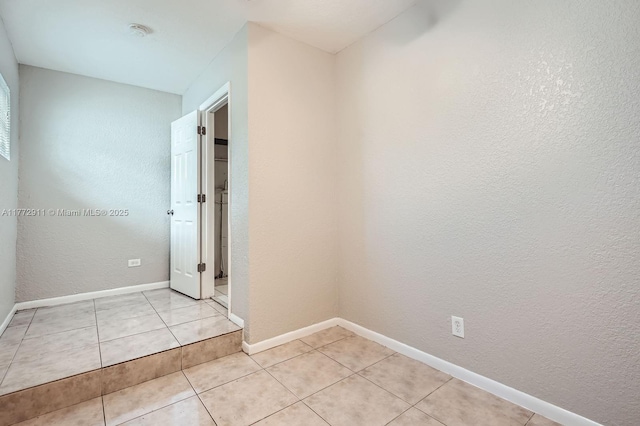 unfurnished room with a textured wall, light tile patterned floors, and baseboards