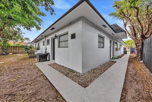 view of side of home with stucco siding, fence, and central air condition unit