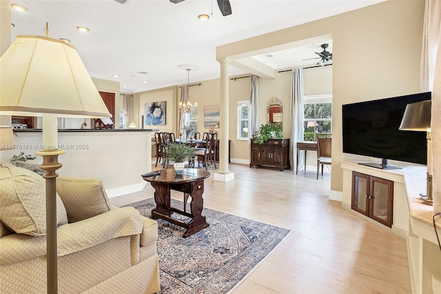 living area with light wood-type flooring, ceiling fan with notable chandelier, and baseboards
