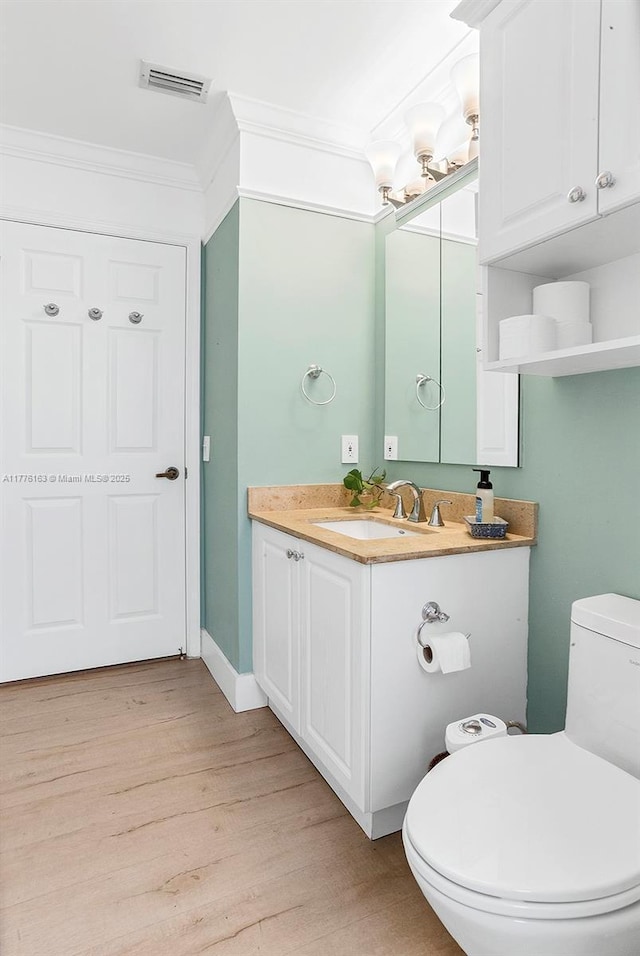 bathroom with visible vents, toilet, crown molding, vanity, and wood finished floors