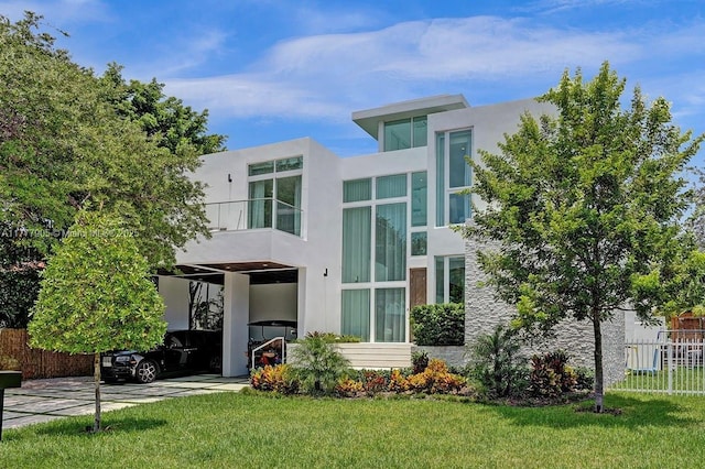 rear view of house with a yard, fence, a balcony, and stucco siding