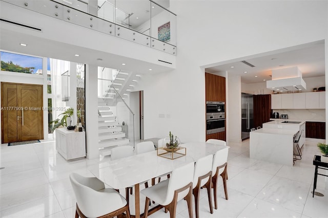 dining area with visible vents, stairs, light tile patterned flooring, and a towering ceiling