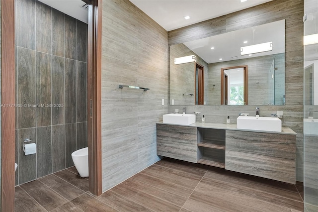 bathroom with double vanity, a shower with door, tile walls, and a sink
