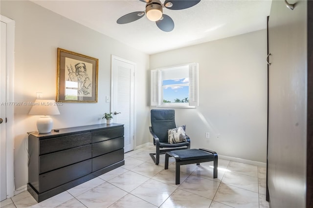 living area with baseboards and ceiling fan