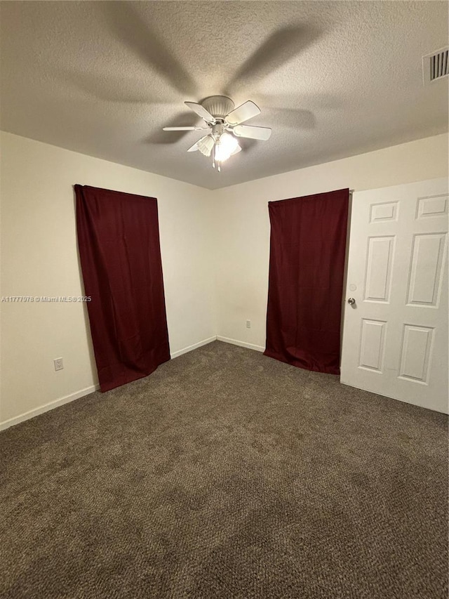 unfurnished bedroom featuring a textured ceiling, baseboards, visible vents, dark carpet, and ceiling fan