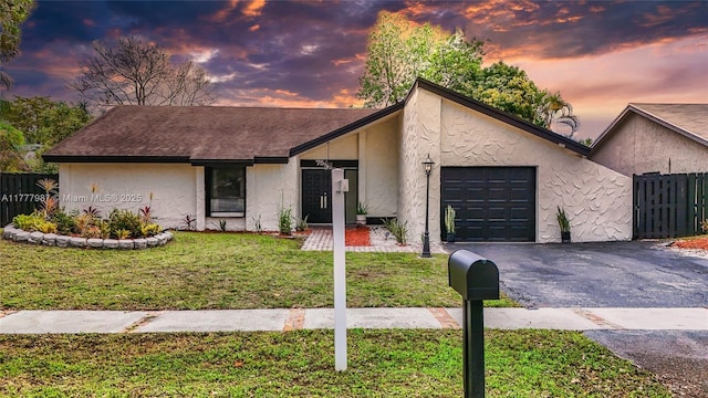 view of front of home featuring aphalt driveway, stucco siding, a lawn, fence, and a garage