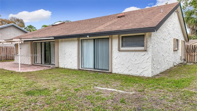 back of house with stucco siding, a lawn, a patio, fence, and a shingled roof