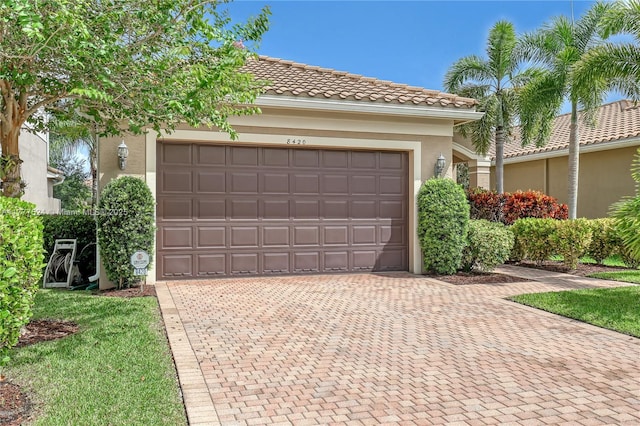 view of front of property with stucco siding, a tiled roof, a garage, and decorative driveway