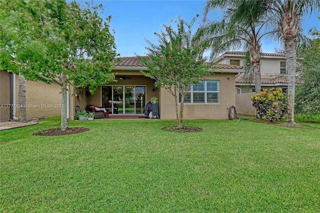 rear view of property with a tile roof, a lawn, a ceiling fan, and stucco siding