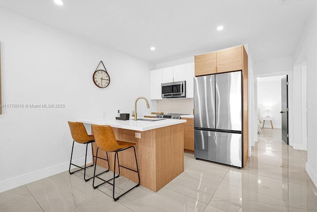 kitchen with light countertops, a sink, a breakfast bar area, tasteful backsplash, and stainless steel appliances
