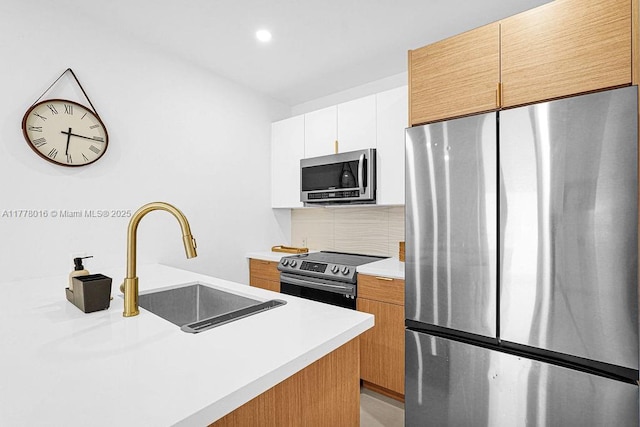kitchen with light countertops, backsplash, a sink, white cabinetry, and stainless steel appliances