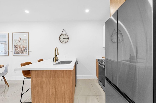 kitchen featuring a kitchen breakfast bar, light countertops, baseboards, a sink, and appliances with stainless steel finishes