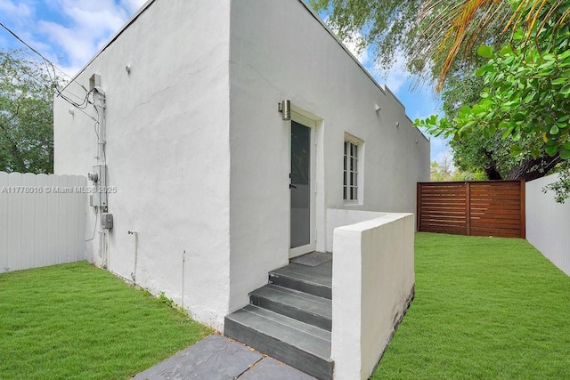 view of side of home featuring stucco siding, fence, and a lawn