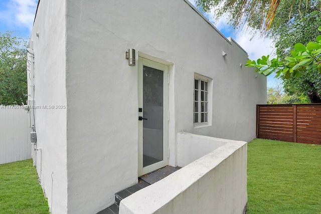 entrance to property with a lawn, fence, and stucco siding