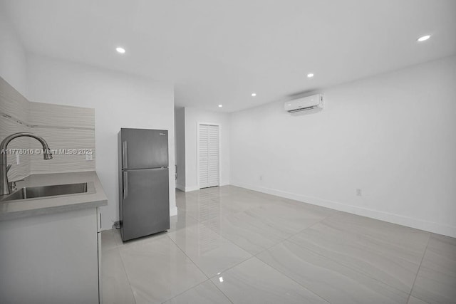 kitchen with light countertops, a sink, freestanding refrigerator, a wall mounted air conditioner, and baseboards