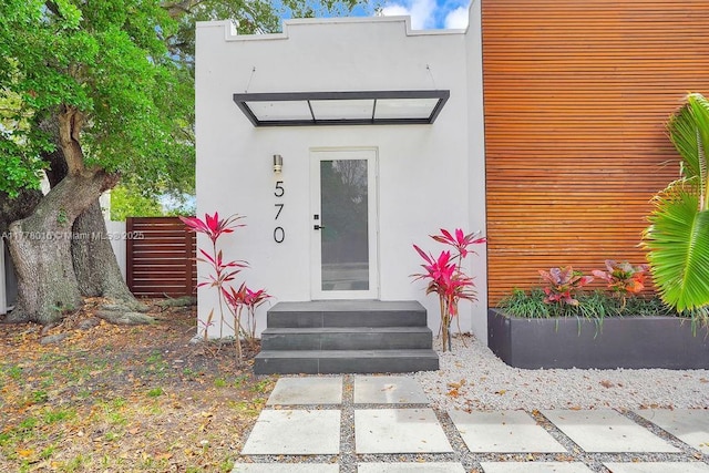 view of exterior entry with stucco siding and fence