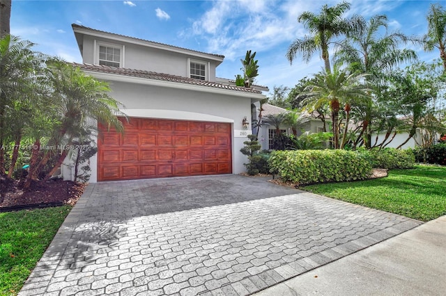 mediterranean / spanish house with a tiled roof, a garage, decorative driveway, and stucco siding