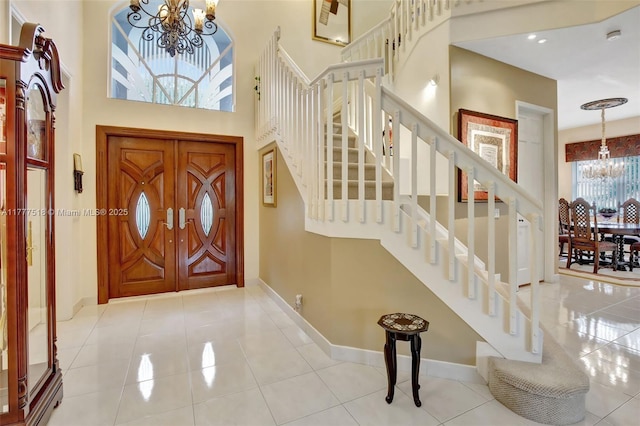 entrance foyer featuring an inviting chandelier, a towering ceiling, tile patterned flooring, stairs, and baseboards