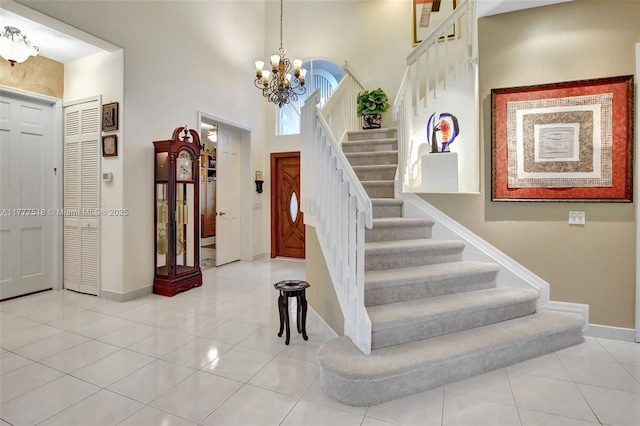 tiled entrance foyer with a chandelier, stairway, a towering ceiling, and baseboards