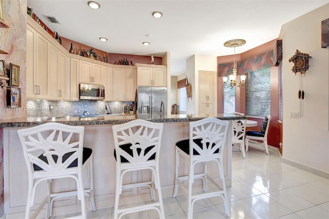kitchen featuring tasteful backsplash, an inviting chandelier, a peninsula, a kitchen bar, and appliances with stainless steel finishes