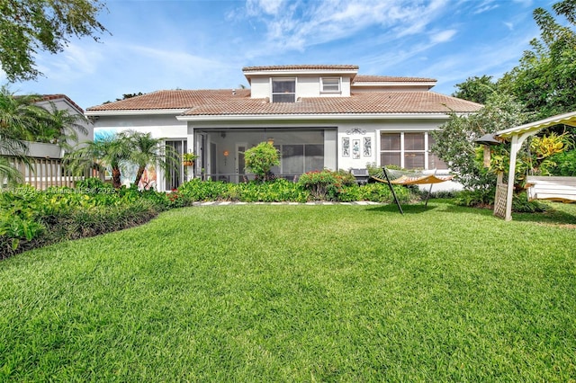back of property with a sunroom, a tiled roof, stucco siding, and a lawn