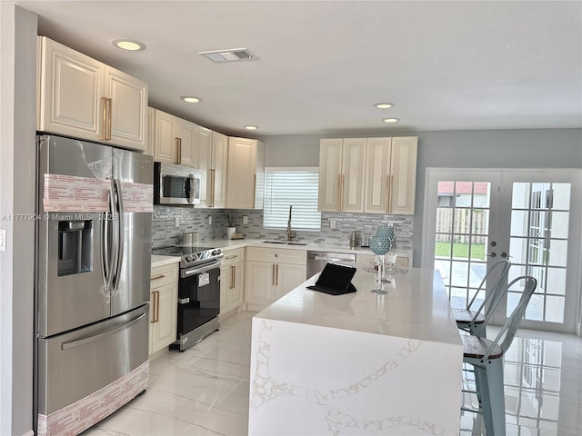 kitchen featuring visible vents, a kitchen island, appliances with stainless steel finishes, a sink, and french doors