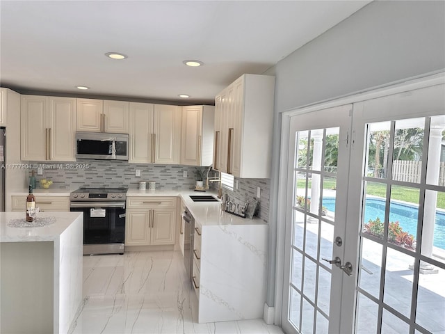 kitchen with backsplash, a sink, appliances with stainless steel finishes, and light stone countertops