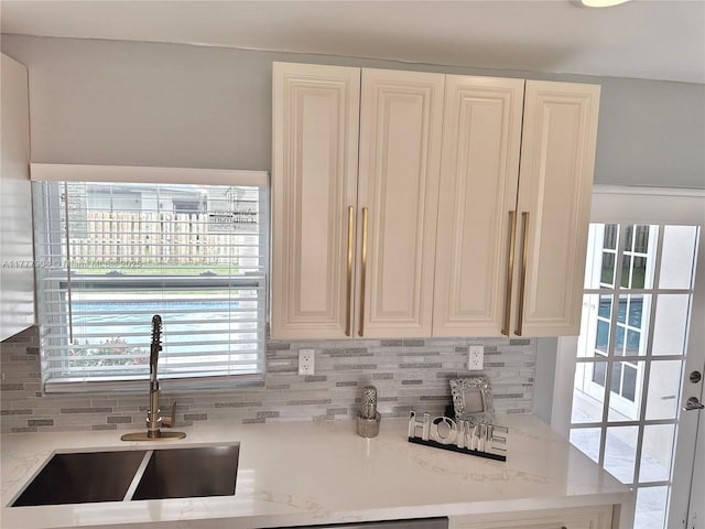 kitchen featuring white cabinetry, a sink, backsplash, and light stone counters