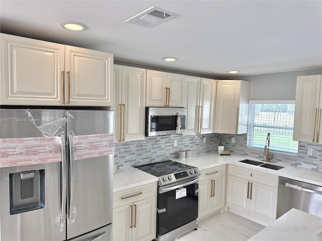 kitchen with a sink, stainless steel appliances, light stone counters, and visible vents